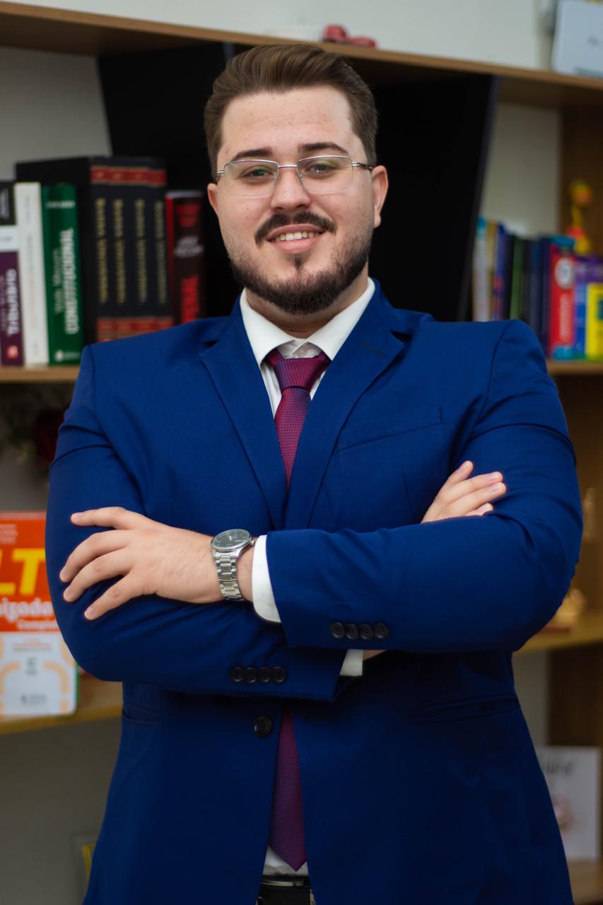Matheus Campos de braços cruzados diante da biblioteca do escritório